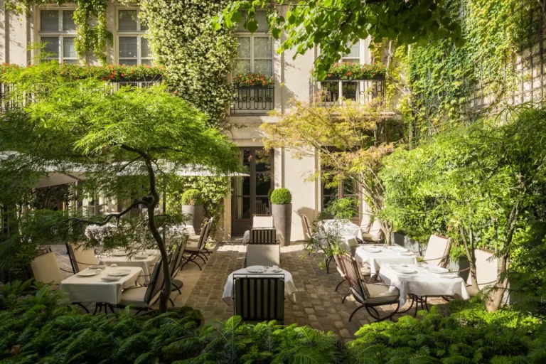 Lush private courtyard garden at Hôtel Pavillon de la Reine in Le Marais, Paris, with outdoor seating surrounded by greenery.
