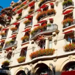 Exterior of Hôtel Plaza Athénée in Paris with red awnings, flower-filled balconies and classic Haussmann-style architecture.