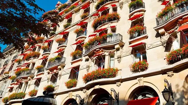Exterior of Hôtel Plaza Athénée in Paris with red awnings, flower-filled balconies and classic Haussmann-style architecture.