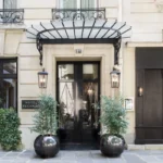 Entrance of Hôtel Récamier in Saint-Germain-des-Prés, Paris, with elegant stone façade, black doors and potted greenery.
