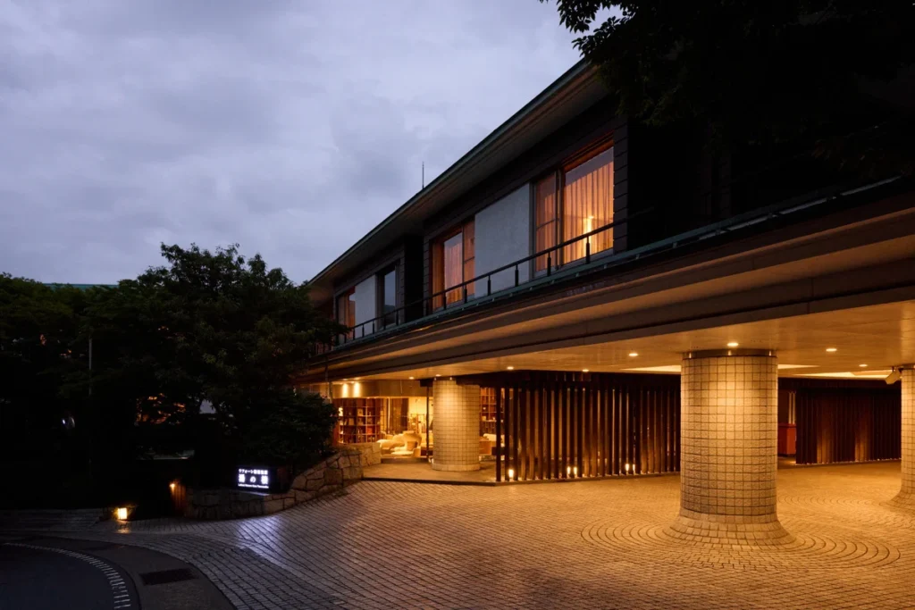 Exterior entrance of Laforet Club Hakone Gora Yunosumika at dusk, featuring modern Japanese architecture, warm lighting, and a tranquil mountain resort atmosphere.