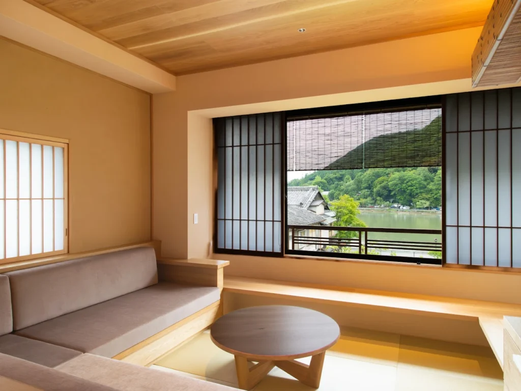 Traditional Japanese-style guest room at Ryotei Rangetsu in Arashiyama, featuring tatami flooring, shoji screens, and scenic views of the Katsura River and surrounding mountains.