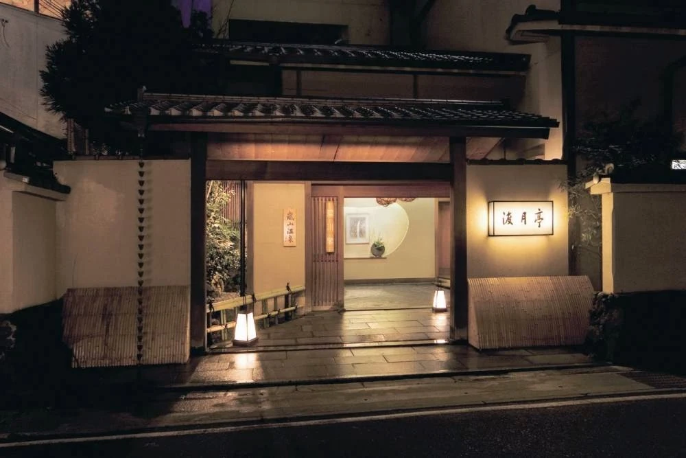 Traditional entrance of Togetsutei Ryokan in Arashiyama, Kyoto, illuminated at night with classic Japanese architecture and warm ambient lighting.