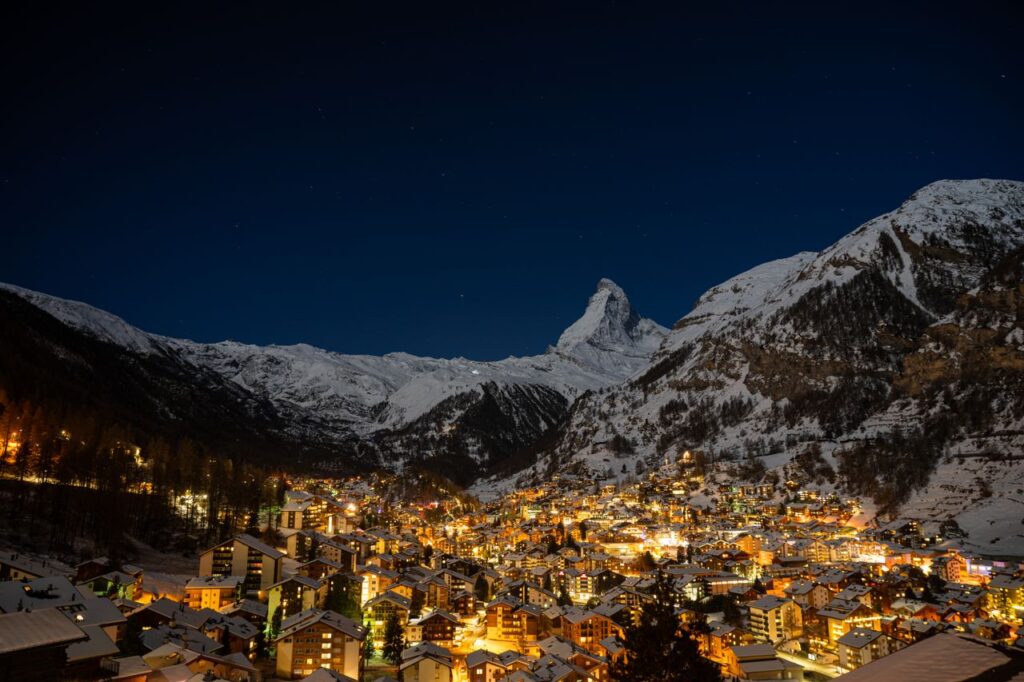 Night view of Zermatt village illuminated by warm lights beneath the snow-covered Matterhorn mountain in the Swiss Alps.