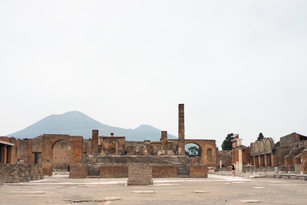 Ancient ruins of Pompeii's forum with Mount Vesuvius rising in the background under an overcast sky in Italy.