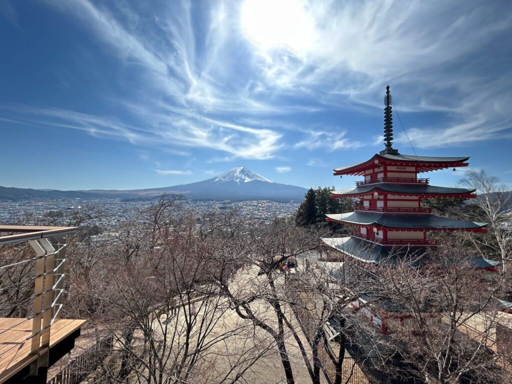 Chureito Pagoda overlooking Fujiyoshida City with Mount Fuji in the background beneath dramatic clouds and blue skies in Yamanashi, Japan.