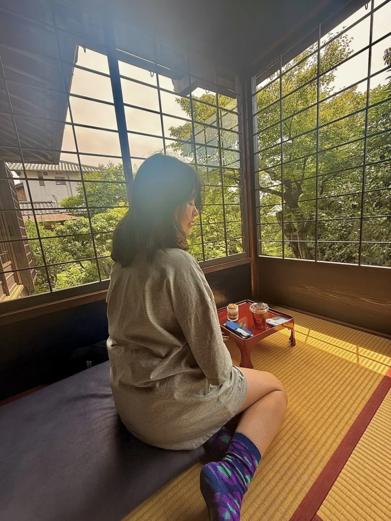 7-Day Osaka, Kyoto and Kobe Itinerary: Food, Shopping and Summer Sights 25 Woman seated on tatami mats beside shoji-style windows overlooking a green Japanese garden in Kyoto.
