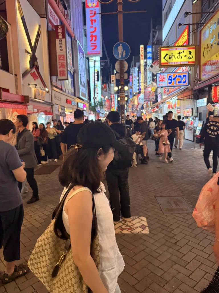 7-Day Osaka, Kyoto and Kobe Itinerary: Food, Shopping and Summer Sights 14 Woman walking through the crowded Dotonbori entertainment district in Osaka at night, surrounded by illuminated restaurant and shopping signs.