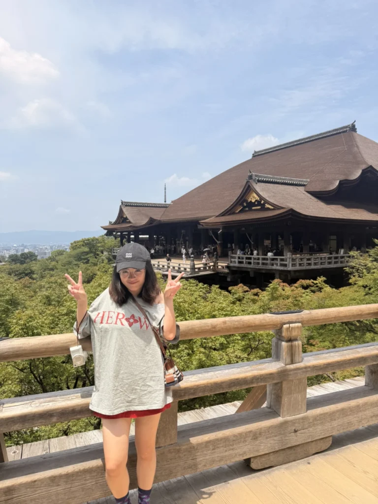 7-Day Osaka, Kyoto and Kobe Itinerary: Food, Shopping and Summer Sights 23 Woman posing on the wooden terrace at Kiyomizu-dera Temple with the main hall and Kyoto city views behind her.