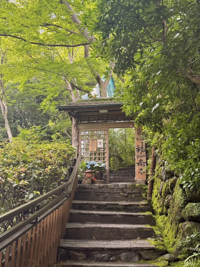Stone staircase leading to the entrance gate of Arashiyama Yusai-tei surrounded by lush greenery