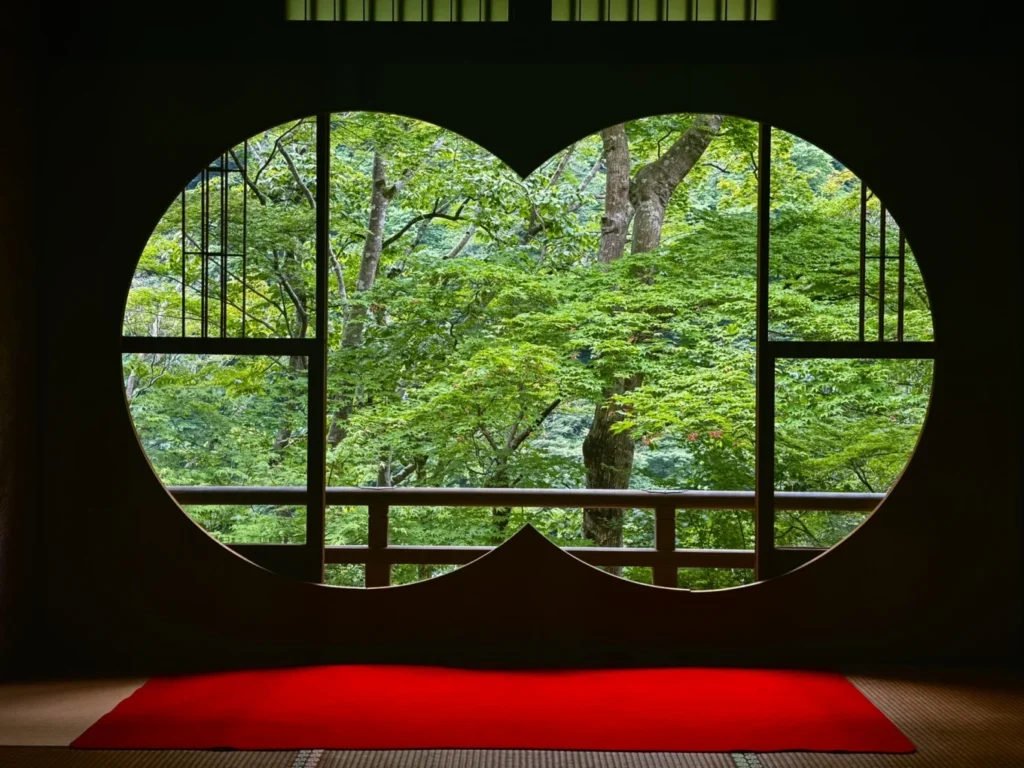 Circular heart-shaped window framing fresh green maple trees at Arashiyama Yusai-tei