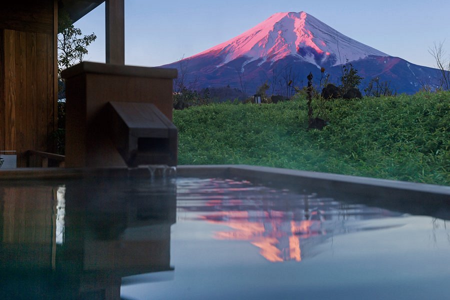 Private open-air onsen at Bself Fuji Villa with a stunning view of Mount Fuji glowing pink at sunrise in Fujiyoshida, Japan.