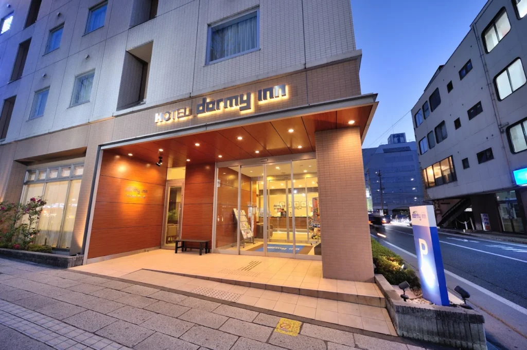 Entrance of Dormy Inn Matsumoto illuminated at dusk, located near Matsumoto Station and known for its natural hot spring facilities.