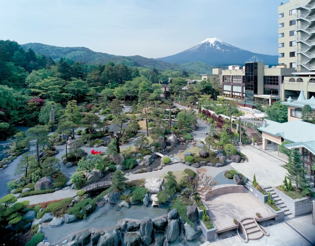 Panoramic view of Fujisan Onsen Hotel Kaneyamaen's traditional Japanese gardens with Mount Fuji rising in the background on a clear day.