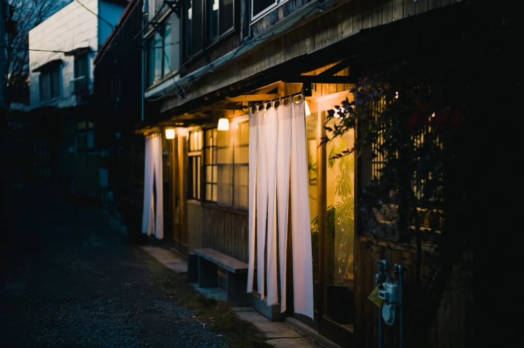 Traditional wooden exterior of Hostel SARUYA in Fujiyoshida, Japan, illuminated at dusk, showcasing its renovated townhouse architecture near Mount Fuji Station.