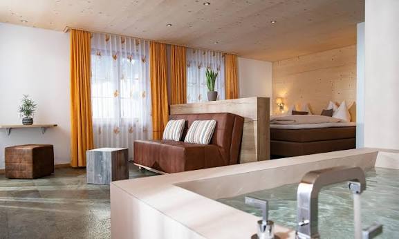 Spacious suite at Hotel Silberhorn in Lauterbrunnen featuring a private in-room whirlpool bathtub, cozy seating area, warm wooden interiors, and a king-sized bed.