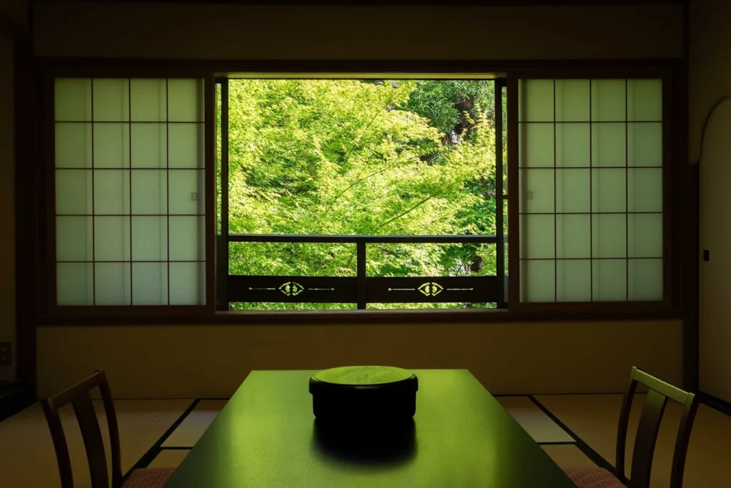 Traditional tatami room at Izumiso Ryokan overlooking lush green gardens through large shoji-framed windows in Asama Onsen, Matsumoto.