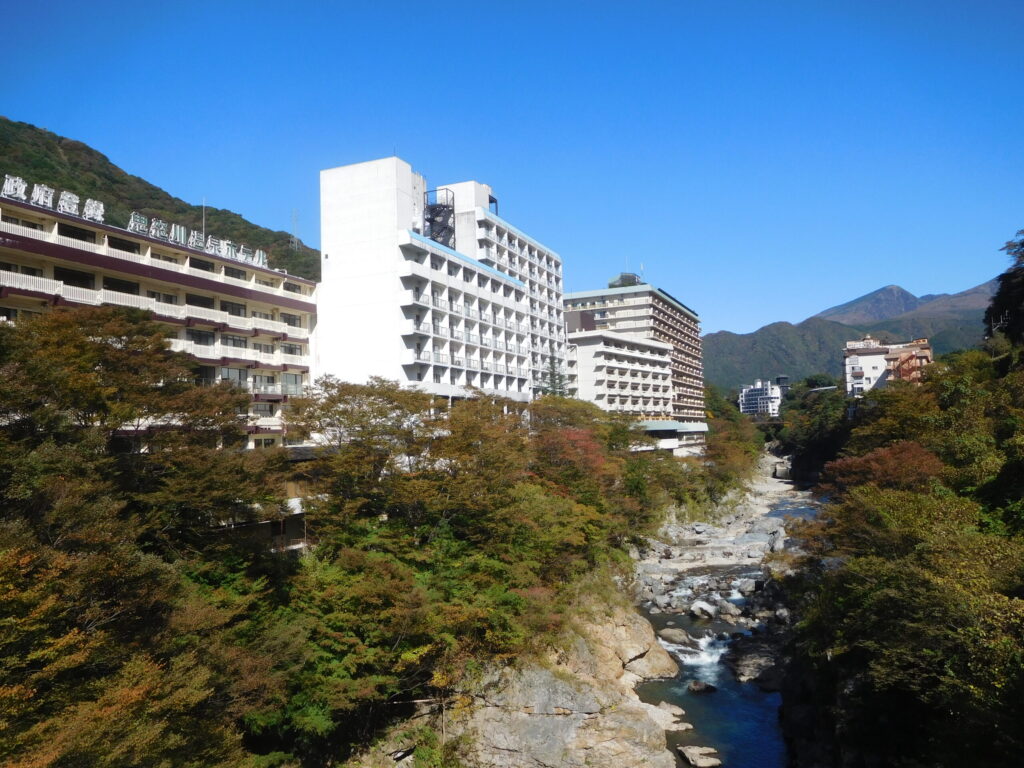Hotels and ryokan along the Kinugawa River in Kinugawa Onsen, Nikko, Japan, surrounded by mountains and autumn foliage.