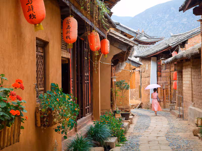 Where to Stay in Dali: 6 Best Areas & Hotels 7 Traditional lane in Longkan village, Dali, lined with earthen houses, red lanterns and flowers, with mountains in the background.
