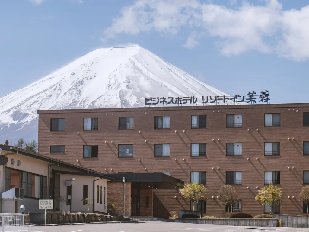 Exterior of Resort Inn Fuyo in Fujiyoshida with snow-capped Mount Fuji towering behind the hotel on a clear day.
