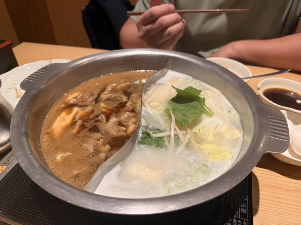 Dual soup pot with sukiyaki and creamy soy milk broth at Shabu Sai AEON Mall Kobe Kita, one of the best all-you-can-eat shabu shabu restaurants near Kobe-Sanda Premium Outlets.
