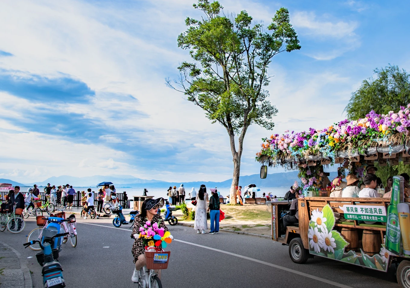 Visitors cycling and walking along the waterfront beside Erhai Lake in Dali, with mountains visible across the water.