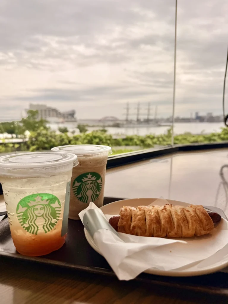 7-Day Osaka, Kyoto and Kobe Itinerary: Food, Shopping and Summer Sights 11 Starbucks drinks and a sausage pastry beside a window overlooking Kobe’s Meriken Park waterfront.