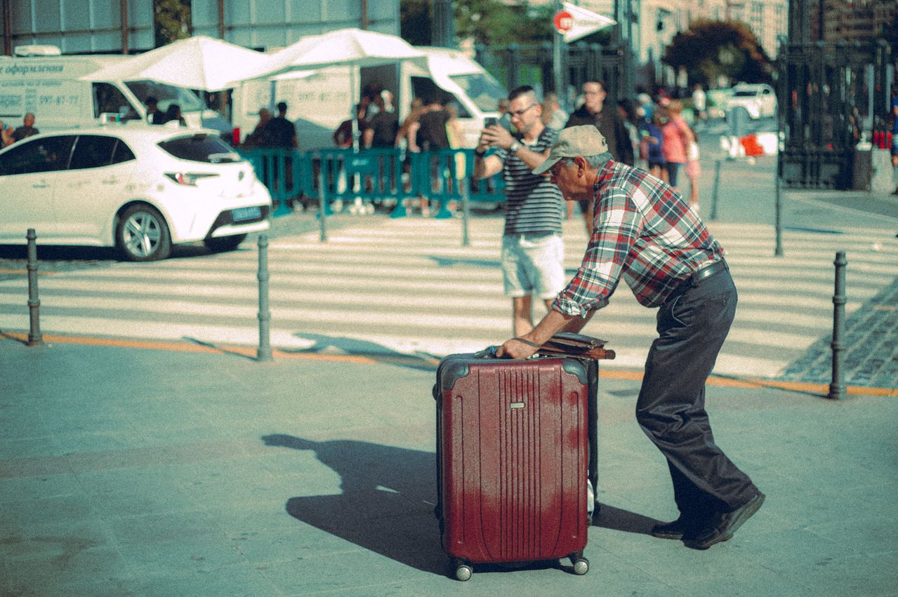 Senior traveler pushing a large red spinner suitcase across a city street
