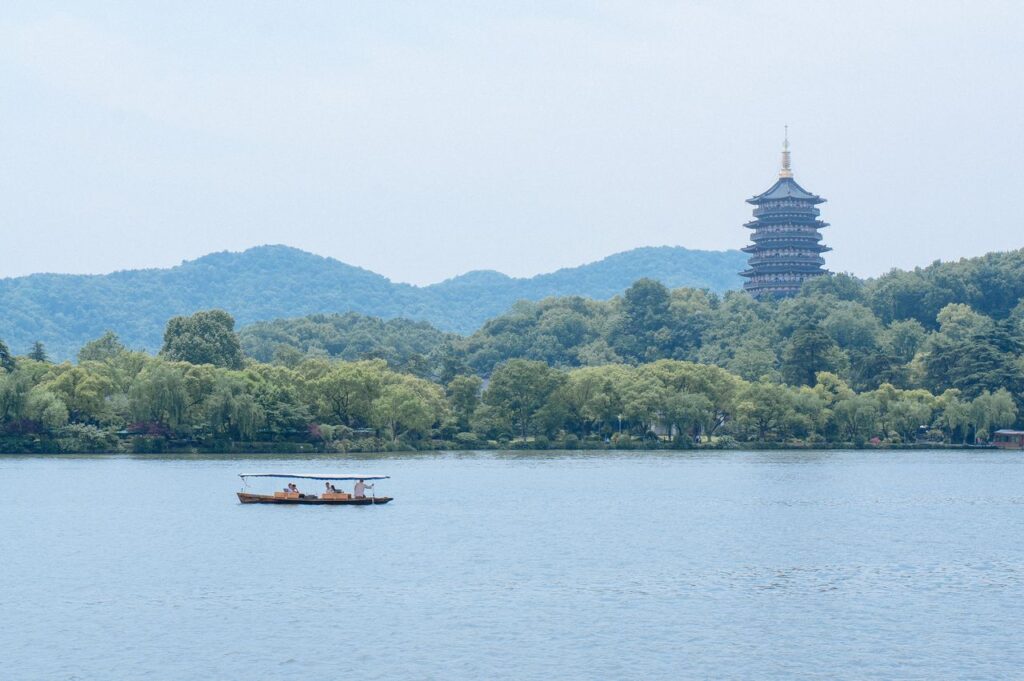Traditional wooden boat sailing across West Lake with Leifeng Pagoda in the background, Hangzhou, China