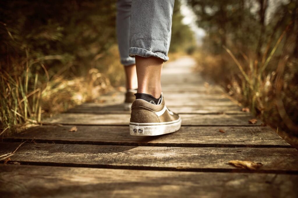 Senior traveler wearing comfortable walking shoes while strolling along a wooden boardwalk, illustrating supportive footwear for long walks and sightseeing.