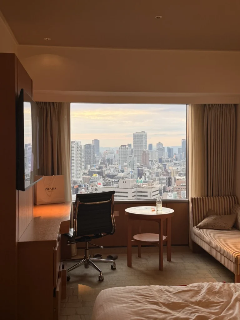 7-Day Osaka, Kyoto and Kobe Itinerary: Food, Shopping and Summer Sights 17 High-floor room at Swissôtel Nankai Osaka with a large window overlooking the Osaka city skyline at sunset.