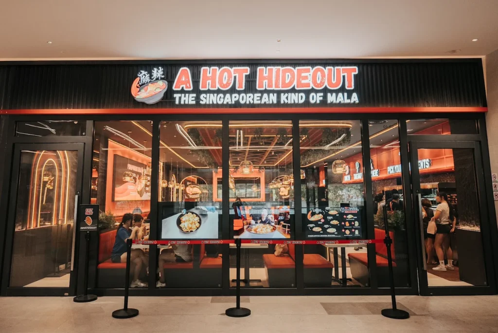 Lentor Modern Food Guide: 17 Best Places To Eat Near Lentor MRT 5 A Hot Hideout mala restaurant storefront at Lentor Modern, featuring an illuminated sign and bright orange-red interior.