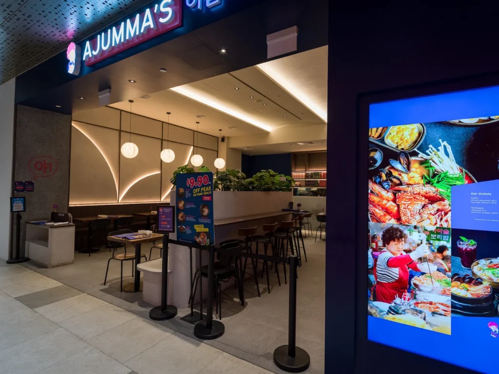 Lentor Modern Food Guide: 17 Best Places To Eat Near Lentor MRT 13 Ajumma’s Korean restaurant entrance at Lentor Modern, featuring illuminated signage, modern seating and a digital menu display.