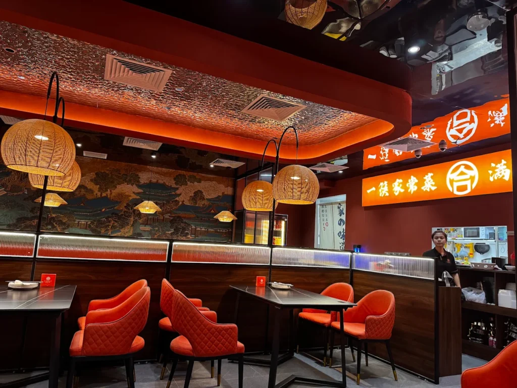 Lentor Modern Food Guide: 17 Best Places To Eat Near Lentor MRT 14 He Jia Huan Chinese restaurant interior at Lentor Modern, featuring orange seating, woven pendant lights and illuminated Chinese signage.