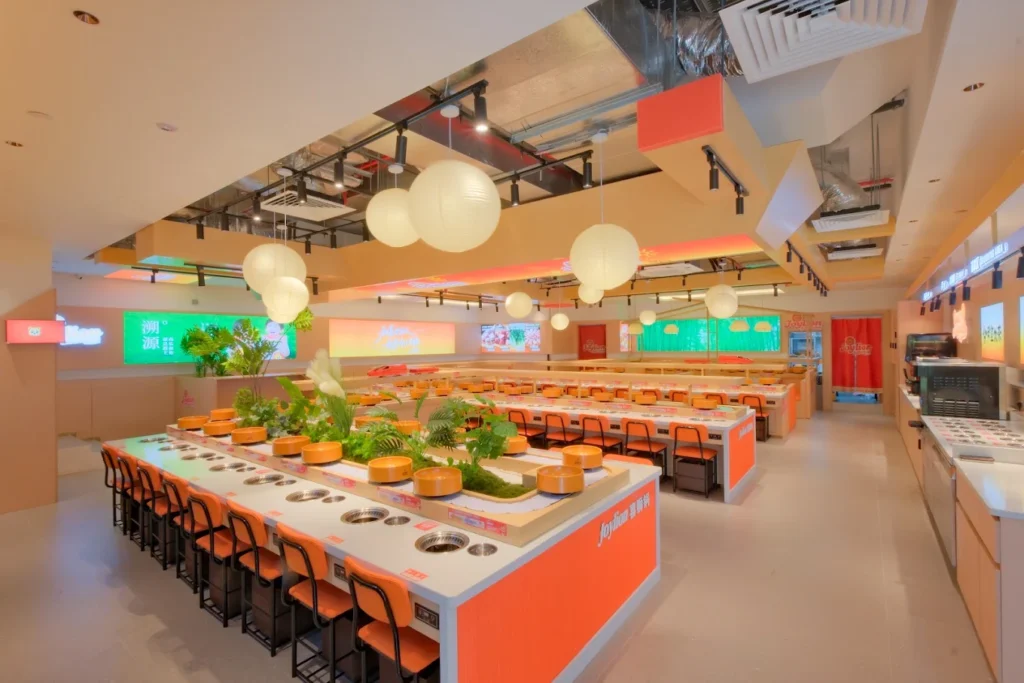 Lentor Modern Food Guide: 17 Best Places To Eat Near Lentor MRT 12 Bright orange interior of Joylion Buffet Hotpot at Lentor Modern, featuring individual hotpot stations and rotating ingredient lanes.
